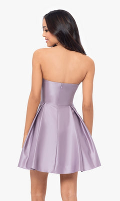 A woman in the Short Strapless Sweetheart Hoco Dress 4914BN, featuring lilac satin, a fit and flare silhouette, sweetheart neckline, and ruched waist, stands with her back to the camera against a plain white background.