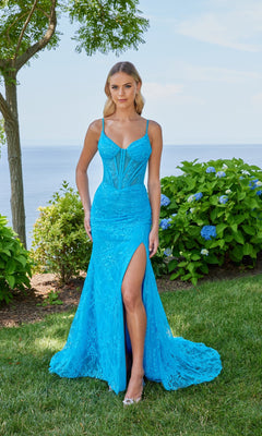 A woman in a turquoise Morilee 49158 long prom dress with a lace corset bodice and high-leg slit stands on grass before green bushes and blue hydrangeas near a body of water.