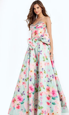A woman models the Jovani 49197 long prom dress, featuring a strapless floral A-line silhouette with a sweetheart neckline, corset bodice, and large waist bow, set against a plain light background.