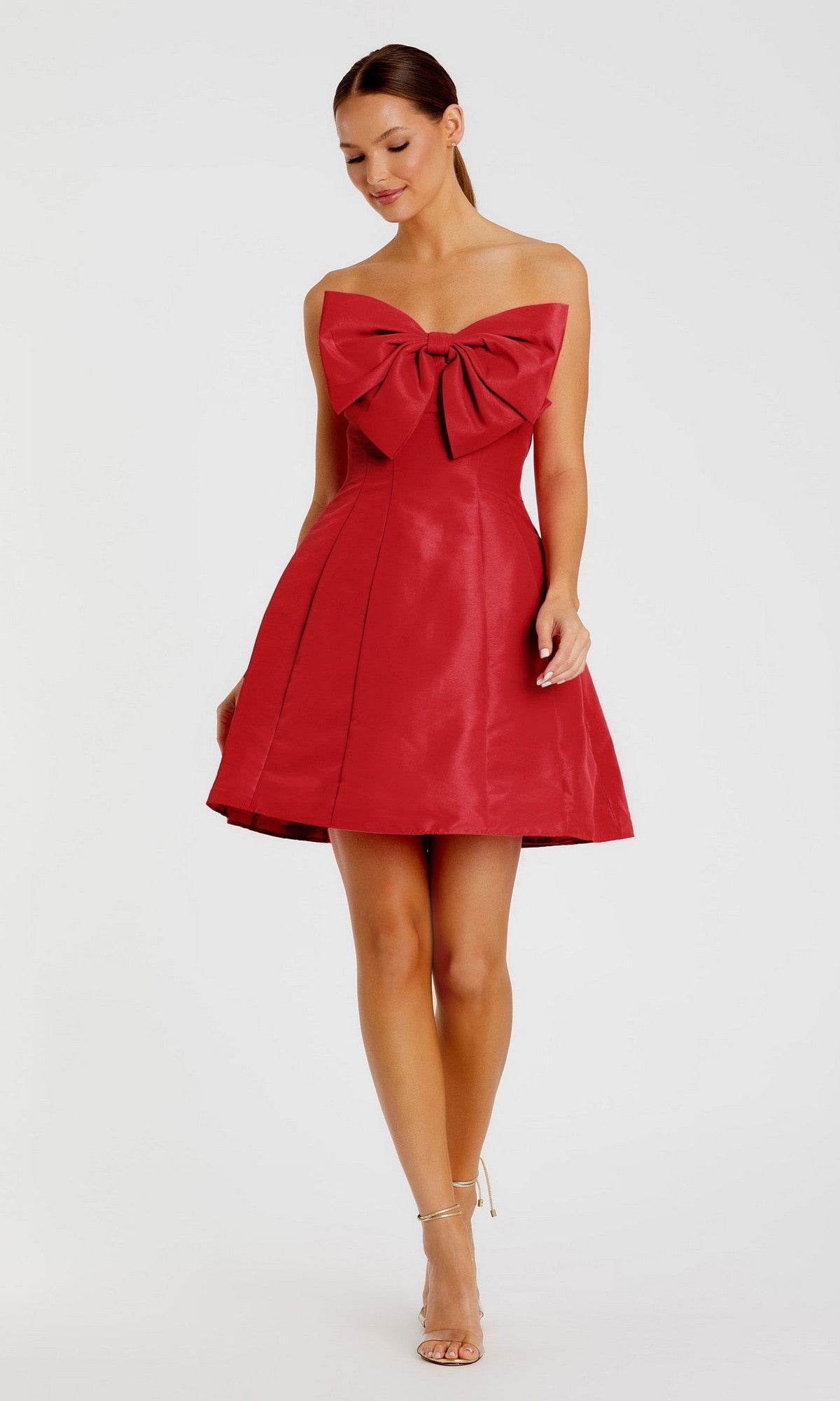 A woman models the Mac Duggal 49210 Strapless Short Bow Party Dress—knee-length, red, with a prominent chest bow—against a plain white background.