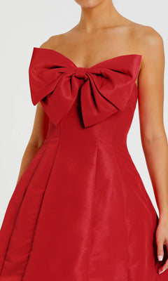 A woman wears the Mac Duggal 49210 Strapless Short Bow Party Dress in vibrant red, showcasing a bold bow detail at the chest for an elegant semi-formal style.