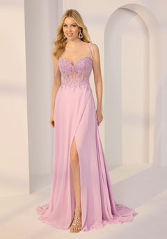 A woman wears the Morilee 49212 long prom dress in peony, featuring a lace corset bodice and chiffon a-line skirt, paired with strappy sandals and earrings indoors.