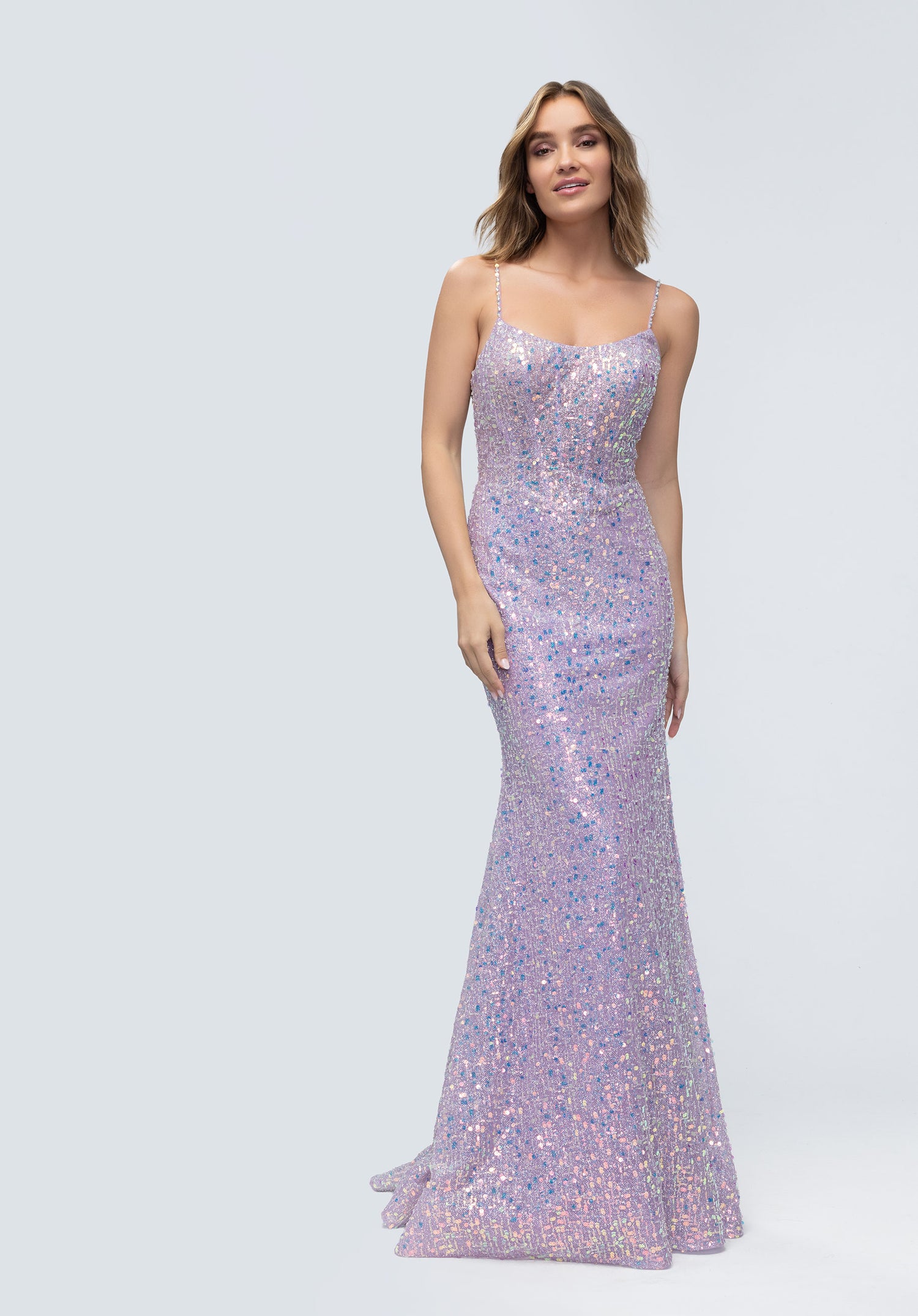 A woman in a floor-length, sleeveless Morilee 49236 long prom dress in light lilac sequin-embroidered tulle with thin straps stands against a light gray background.