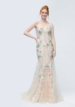 A woman stands against a plain light background wearing the Morilee 49244 long prom dress in green/blush, featuring thin straps and floral embroidery on sheer fabric.