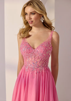 A woman stands indoors looking to the side, wearing the Morilee 49250 long prom dress—a sleeveless pink lace gown featuring floral embroidery and delicate appliqué.