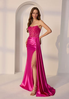 A woman stands before a white arched backdrop wearing the Morilee 49257 long prom dress, featuring a strapless sequined bodice and high slit.
