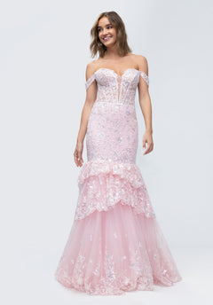 A woman in the Morilee 49274 Long Prom Dress—an off-shoulder, light pink mermaid gown with lace corset, floral accents, and a tiered tulle skirt—stands against a plain background, smiling.