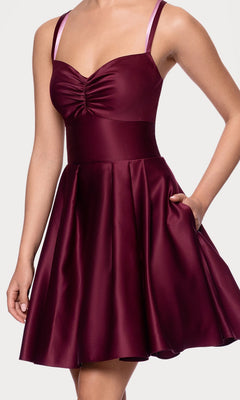 A woman wears the Hunter Green Mini Hoco Dress (Blondie Nites 4927BN), a sleeveless satin A-line homecoming dress with a fitted ruched bodice, flared skirt, and one hand in her pocket.
