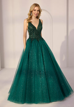 A woman stands in a softly lit room wearing the Morilee 49290 Long Prom Dress in Emerald, featuring a beaded bodice and a glitter tulle skirt.
