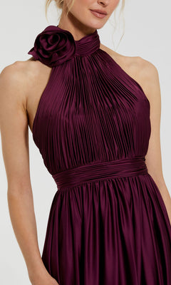 Woman wearing the Mac Duggal 49333 High-Neck Halter Formal Dress, a long pleated burgundy satin gown with a statement neck flower and an elegant open-back silhouette.