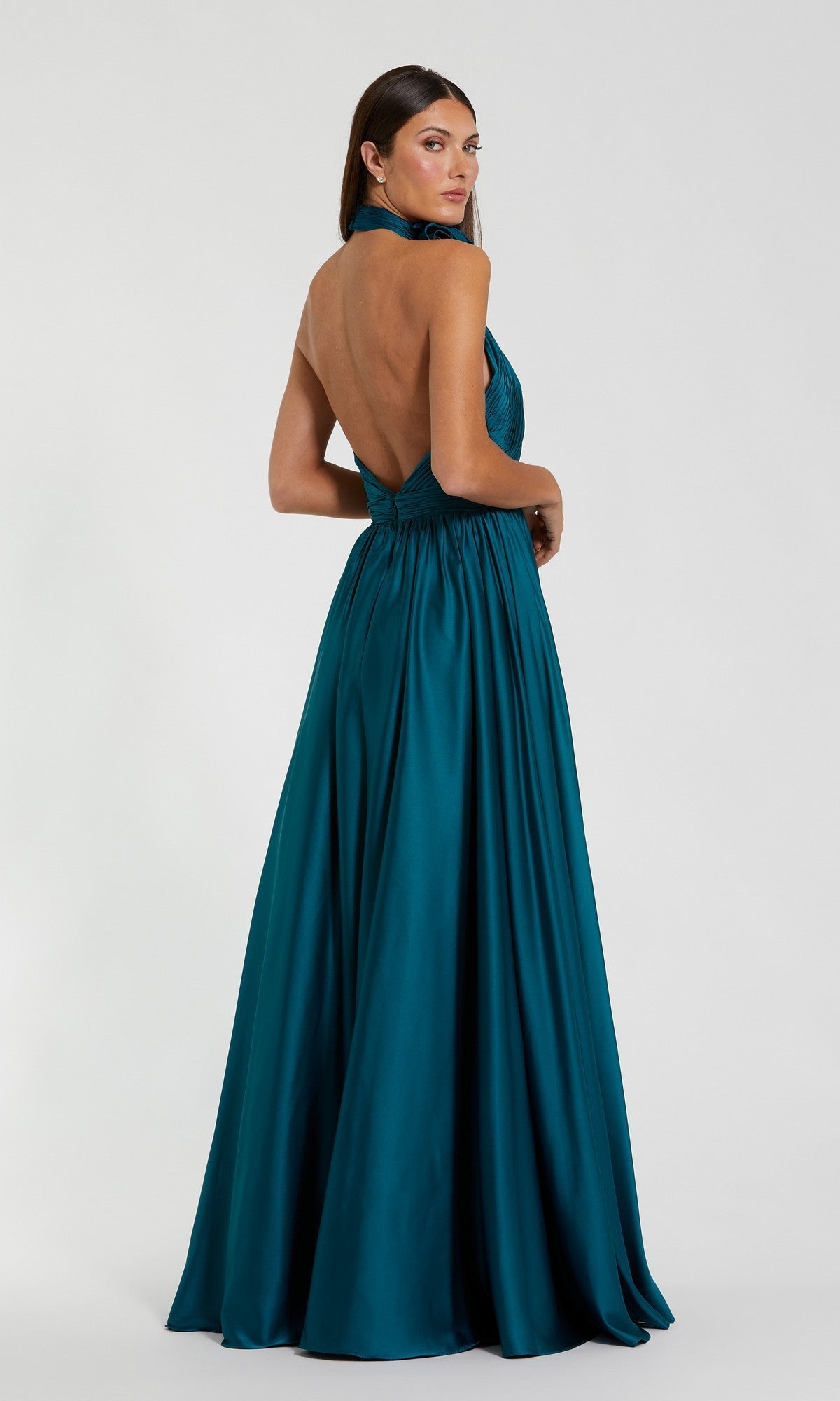 A woman wearing the Mac Duggal 49333 high-neck halter formal dress in teal, featuring an open back and satin finish, stands against a plain white background.