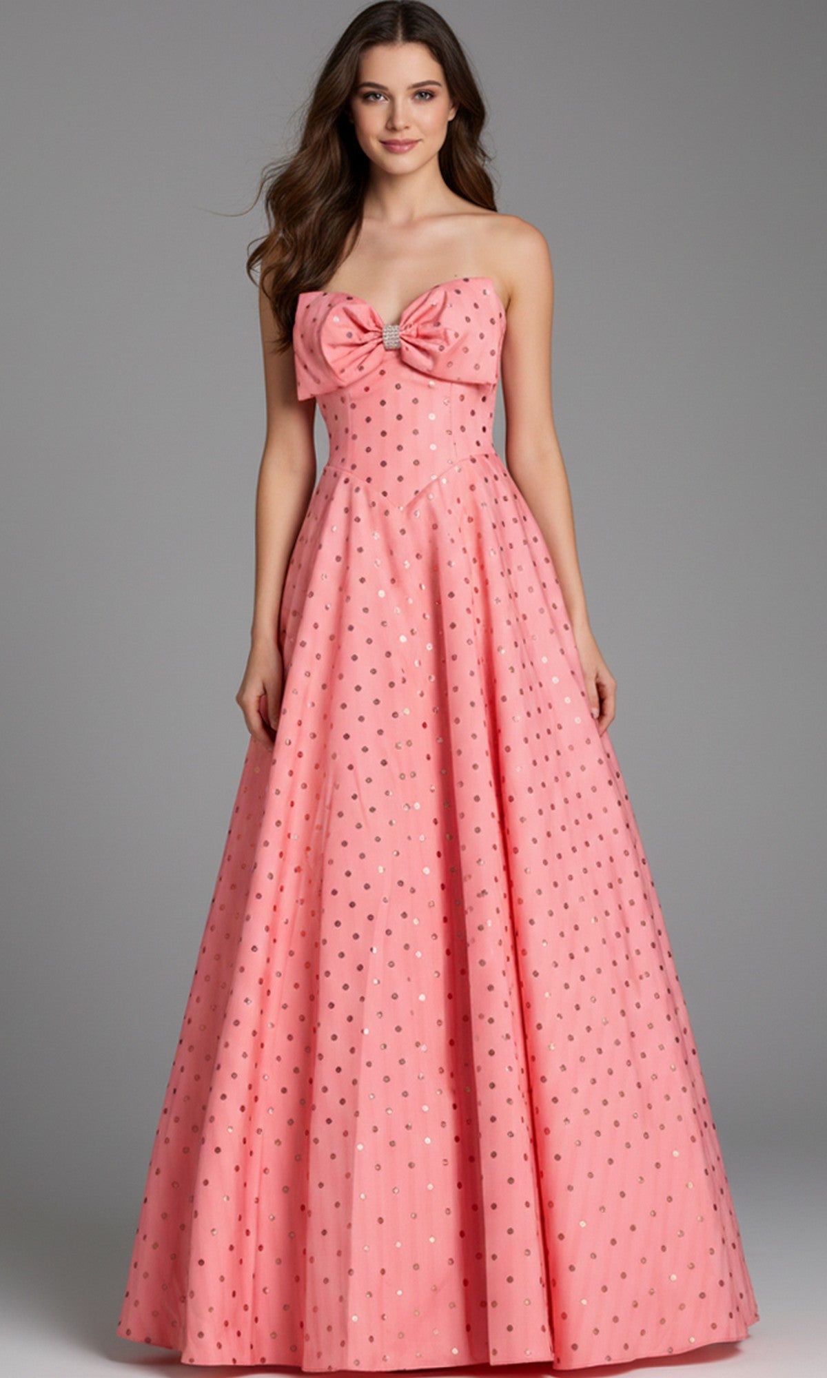 A woman wearing the Jovani 49340 long prom dress in salmon, a strapless ballgown with a large chest bow and small metallic polka dots.