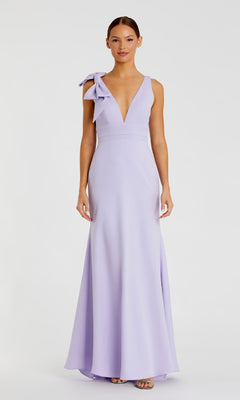A woman models the Mac Duggal 49454 Shoulder-Bow Long Prom Dress in lavender, featuring a deep V-neckline, large shoulder bow, and elegant A-line silhouette, posed against a plain white background.