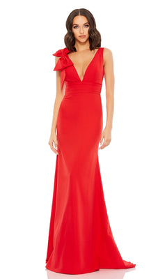 A woman wears the Mac Duggal 49454 Shoulder-Bow Long Prom Dress—a floor-length, sleeveless red gown with a deep V-neckline and a statement shoulder bow—posing against a plain white background, radiating elegance and sophistication.