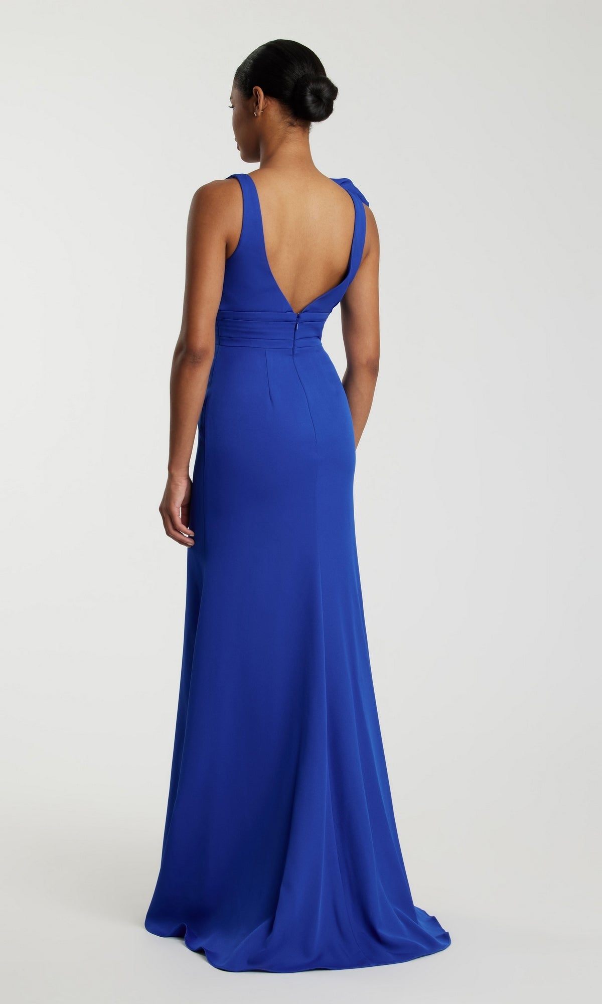 A woman faces away, wearing the Mac Duggal 49454 Shoulder-Bow Long Prom Dress—a royal blue sleeveless gown with a fitted waist, deep V-back, and elegant floor-length skirt.