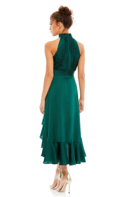 A woman in a sleeveless, emerald green Mac Duggal 49488 high-low wedding guest dress with a halter neck and ruffled hem is seen from the back, paired with gold high-heeled shoes.