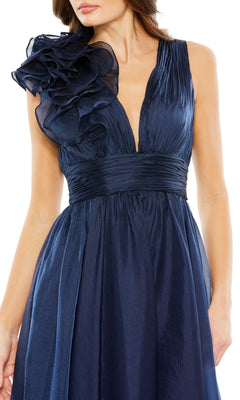A woman wearing the Short Ruched Wedding-Guest Dress (Mac Duggal 49494), featuring a sleeveless deep blue design with a pleated bodice, ruched waistband, and a large ruffled detail on the left shoulder.