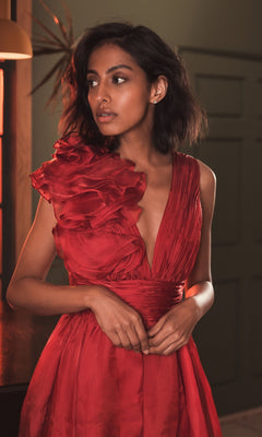 Wearing the Mac Duggal 49494, a short ruched wedding-guest dress with a deep neckline and one-shoulder ruffle, a woman stands indoors looking to the side—a stunning choice for any wedding celebration.
