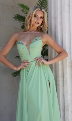 A woman stands by a column, posing with one hand on her hip, wearing the Jovani 49536 long formal dress—a strapless, light green chiffon gown featuring jeweled details and a crystal-embellished trim.