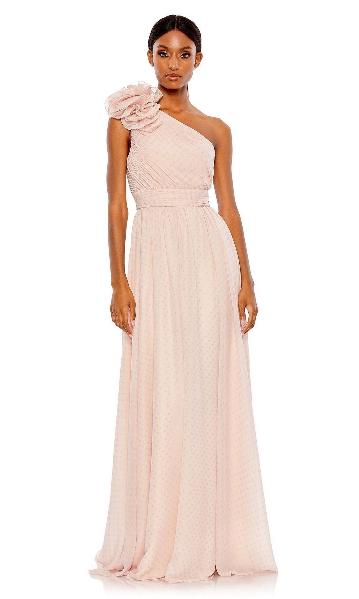 A woman wears the Mac Duggal 49536, a one-shoulder long formal dress in light pink with a floral accent and a textured, flowing floor-length skirt.