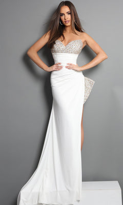 A woman poses against a gray wall wearing the Long Formal Dress: Jovani 49577 in Off White—a striking column gown featuring a strapless crepe silhouette, sequined bodice with side embellishment, thigh-high slit, and floor-length skirt. The crystal-embellished sweetheart neckline provides an extra touch of elegance to this formal look.