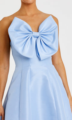 A woman wearing the Mac Duggal 49605, a light blue, strapless tea-length wedding-guest dress featuring a large bow detail on the chest.