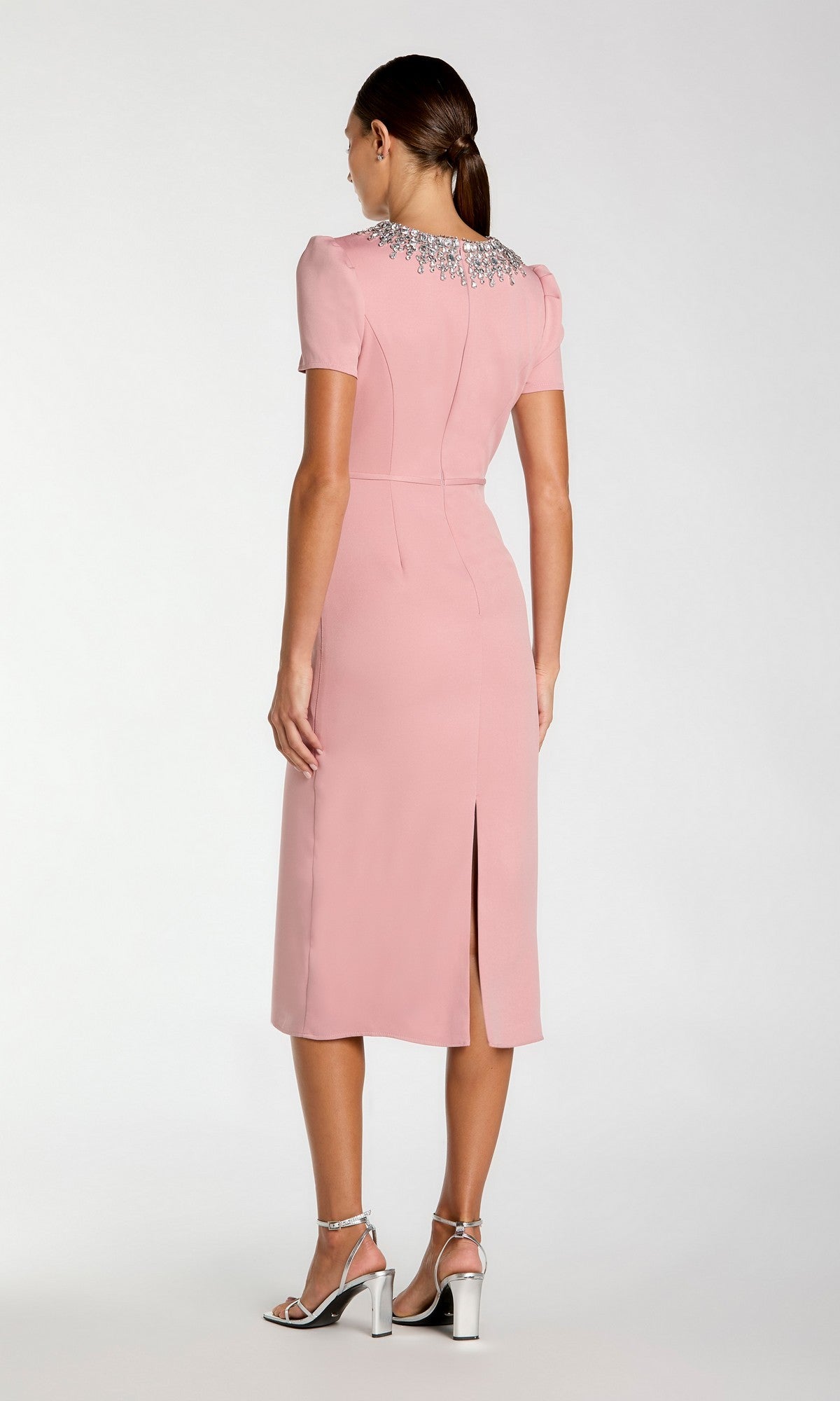Woman wearing the Mac Duggal 49606 short sleeve tea-length party dress in light pink, featuring a beaded collar and back slit, paired with silver high-heeled sandals, is seen facing away from the camera.