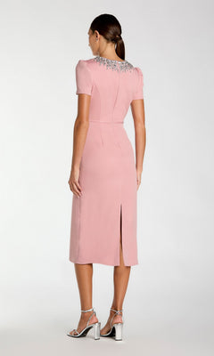 Woman wearing the Mac Duggal 49606 short sleeve tea-length party dress in light pink, featuring a beaded collar and back slit, paired with silver high-heeled sandals, is seen facing away from the camera.