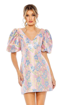A woman faces forward in the Short Homecoming Dress 49622 by Mac Duggal—a pastel pink floral print dress with blue and yellow blooms and puffed short sleeves.