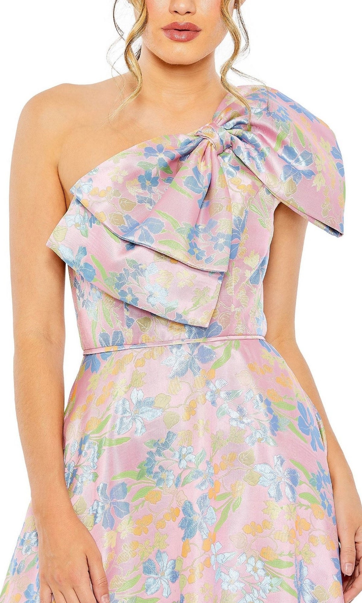 A woman wears Long Formal Dress 49623 by Mac Duggal, a one-shoulder A-line tea length dress in shiny, textured pink pastel fabric with delicate floral print and a large bow.
