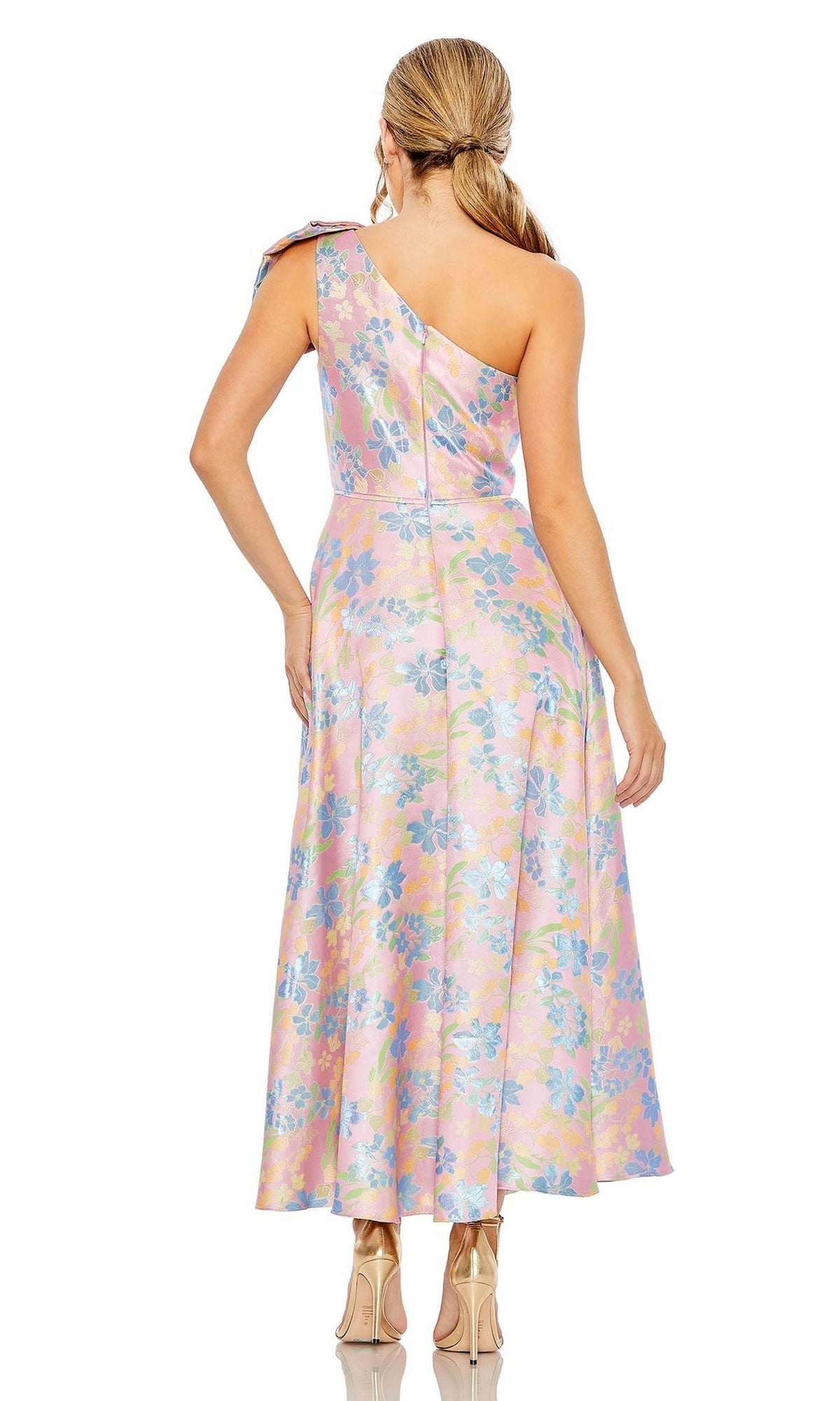 A woman stands facing away from the camera in the Mac Duggal Long Formal Dress 49623—a shiny, pink pastel one-shoulder gown with an A-line skirt—paired with nude heels.