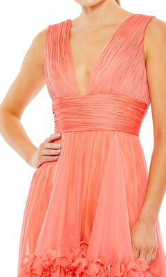 A person wearing the Short Wedding Guest Dress 49635 by Mac Duggal, a sleeveless coral pink knee-length dress with ruching, pleats, a deep V-neckline, and a fitted waist.