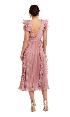 A woman stands facing away, wearing the Short Wedding Guest Dress 49675 by Mac Duggal—a rose pink chiffon midi dress with ruffle cap sleeves, pleated details—and metallic high-heeled shoes.