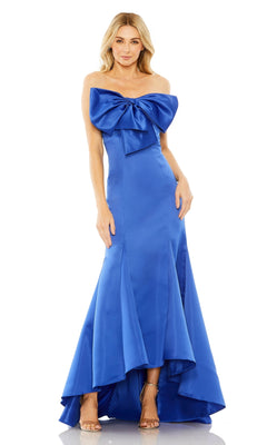 A woman models the Mac Duggal 49701 Strapless Mermaid Formal Dress—a floor-length royal blue evening gown with a large bow on the bodice—standing against a white background.