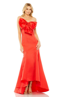 A woman stands poised against a white background, modeling the Strapless Mermaid Formal Dress: Mac Duggal 49701 in vibrant red with a large bow detail on the bodice—an elegant evening gown.