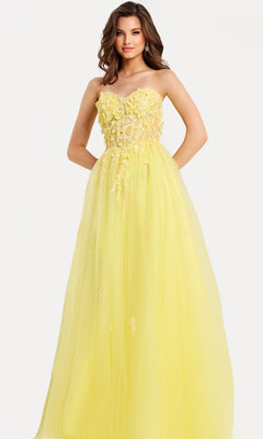 A woman models the yellow Jovani 49704 long prom dress, featuring a strapless floral-embellished bodice and flowing tulle A-line skirt, standing against a plain white background.