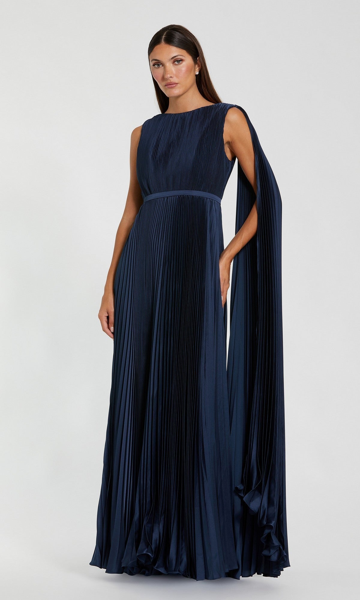 A woman stands wearing a floor-length, sleeveless Mac Duggal 49716 formal gown in sage green, featuring an asymmetrical draped detail on one shoulder and elegant pleats.