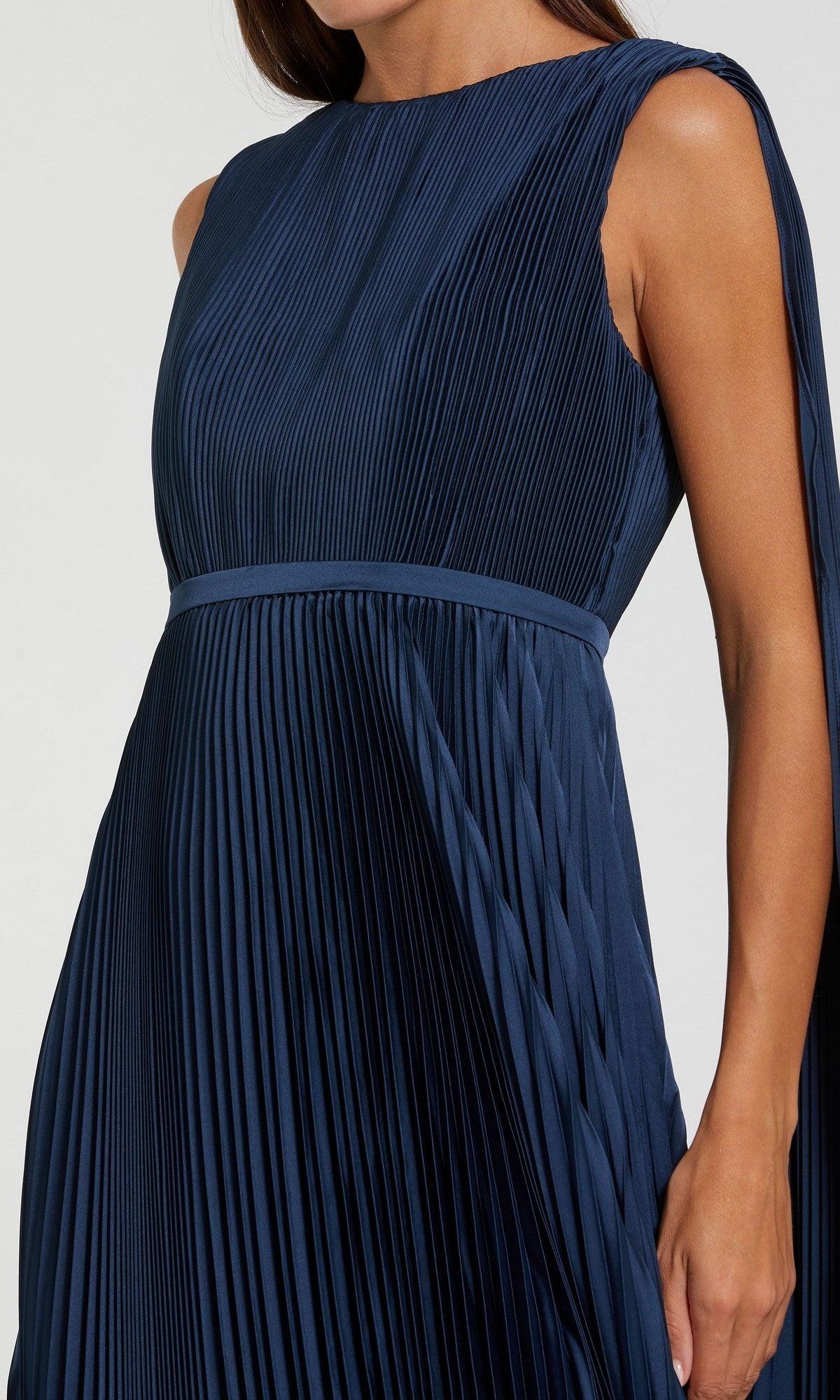 A person wearing a sleeveless, sage green, pleated long formal dress with a fitted waistband—an elegant style inspired by the Mac Duggal 49716 gown.