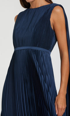 A person wearing a sleeveless, sage green, pleated long formal dress with a fitted waistband—an elegant style inspired by the Mac Duggal 49716 gown.