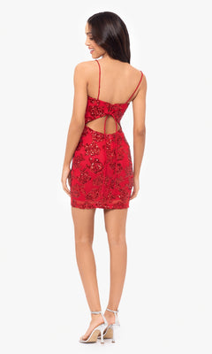 Woman in the Cut-Out Short Red Glitter Hoco Dress 4971BN, featuring a backless design and spaghetti straps, paired with white high-heeled sandals, stands facing away from the camera.