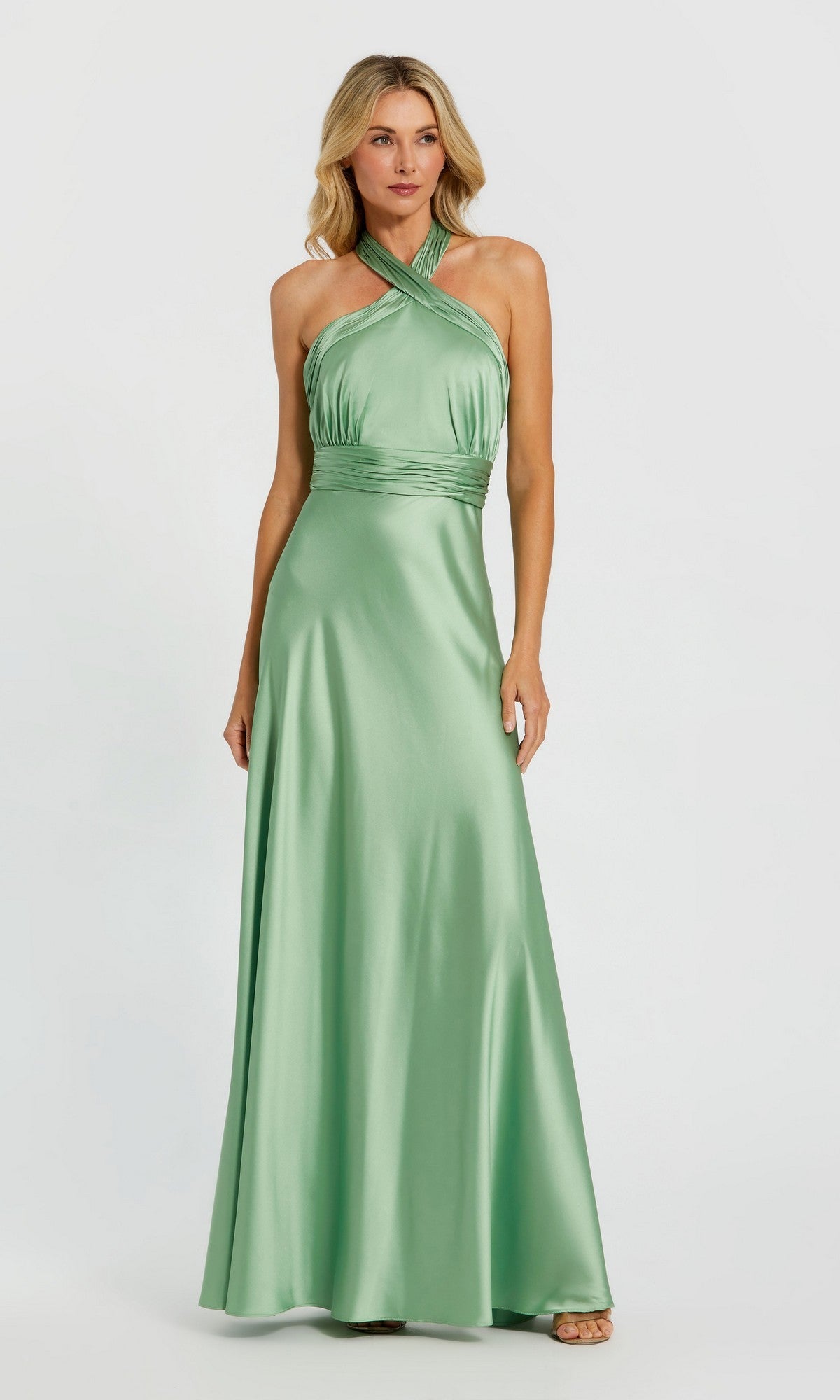 A woman in the Mac Duggal 49728 Long Formal Dress in sage, featuring a halter neck and fitted waist, stands against a plain light background.