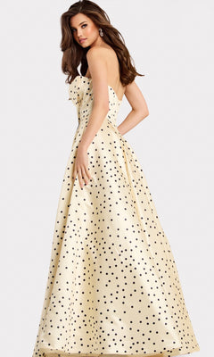 A woman wearing the Jovani 49775, a cream floor-length strapless satin prom dress with black polka dots, stands looking over her shoulder against a plain background.