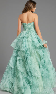 A woman faces away from the camera in a Jovani 49777 Strapless Green Watercolor Prom Gown. The long A-line dress features layered mint green fabric with a delicate floral pattern, all set against a gray background for an elegant look.