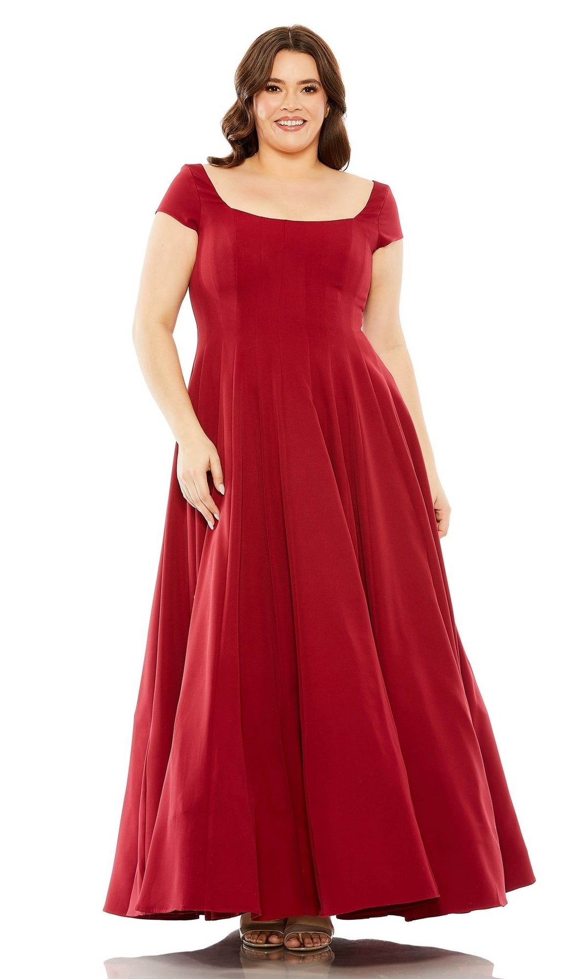 A woman stands facing forward and smiling in a floor-length, short-sleeved red Mac Duggal Plus-Size Simple Long Formal Dress 49783W.