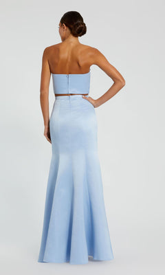 A woman shown from the back wears the Mac Duggal 49832 Strapless Two-Piece Prom Gown, featuring a fitted bodice and flared mermaid skirt in light blue, floor-length and elegant.