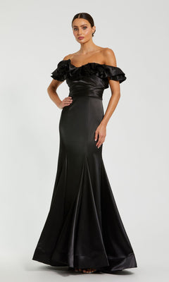 A woman wears the Mac Duggal 49834 Ruffled Long Satin Prom Dress—an off-the-shoulder, floor-length black mermaid gown with ruffled sleeves—standing against a plain light background.