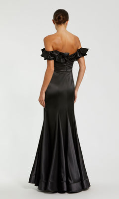 A woman faces away in the Mac Duggal 49834 Ruffled Long Satin Prom Dress, showcasing its ruffled off-the-shoulder neckline and fitted bodice of this elegant formal gown.