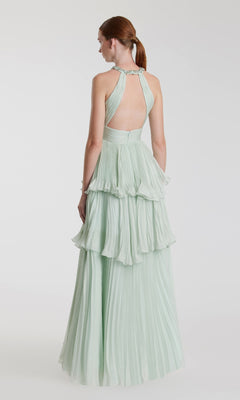 A red-haired woman in a low ponytail wears the Mac Duggal 49835 long mint green formal dress, featuring a backless halter-neck and tiered pleats, as she stands against a plain white background.