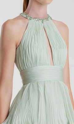A woman in the Mac Duggal 49835 long mint green formal dress, featuring pleats, a jeweled neckline, and wide waistband; shown from shoulders to waist.