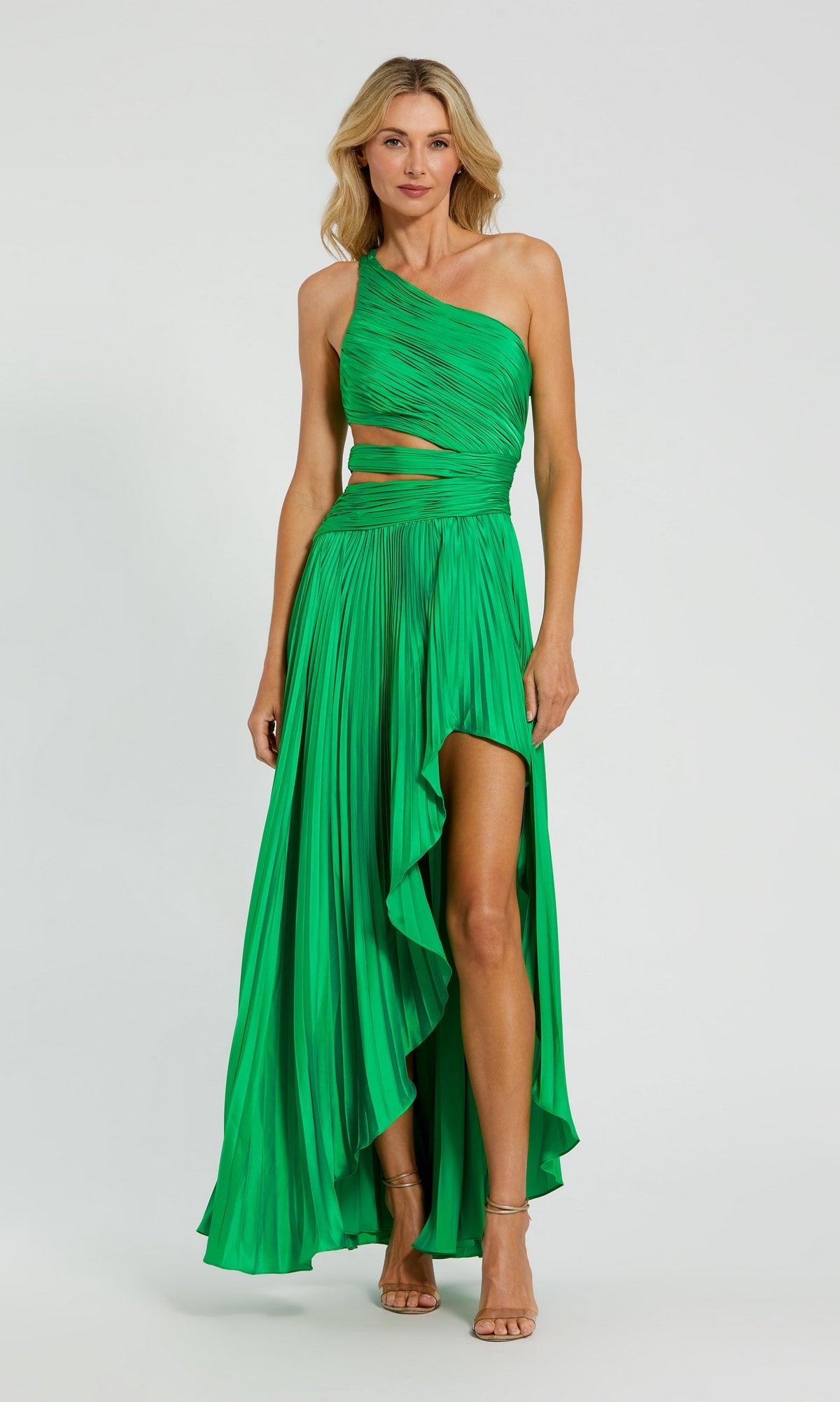 A woman wears the Mac Duggal 49837 High-Low Pleated Formal Dress, featuring a bright green color, cut-out one-shoulder design, pleats, and a high-low hem, as she stands against a plain background.